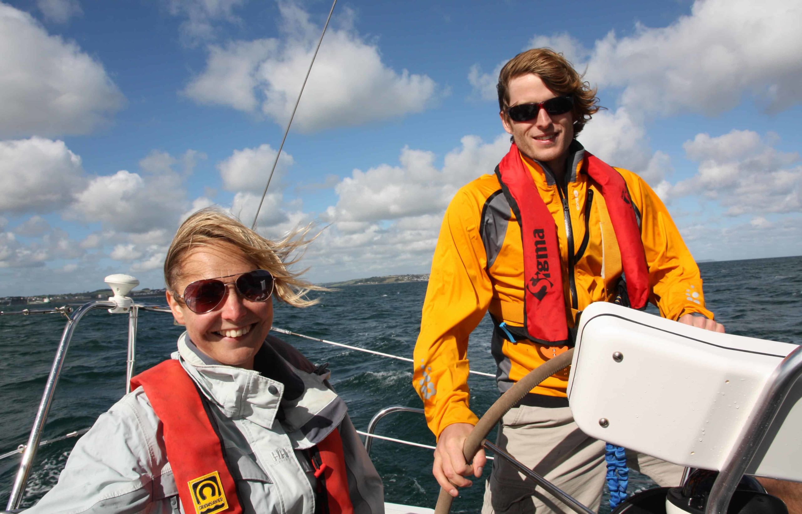 Yacht delivery crew smiling as they sail along the cornish coast