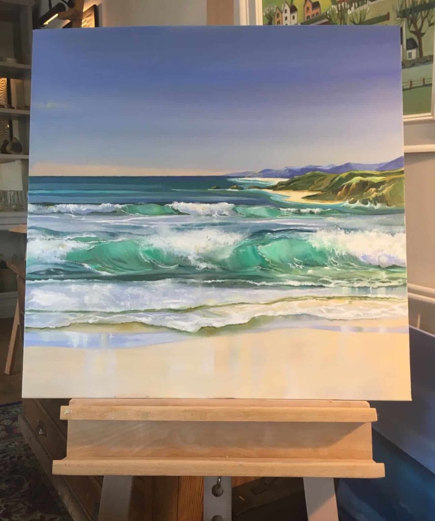 Carolyn Tyrer art work on display on easel. The painting is of waves crashing on a beach.