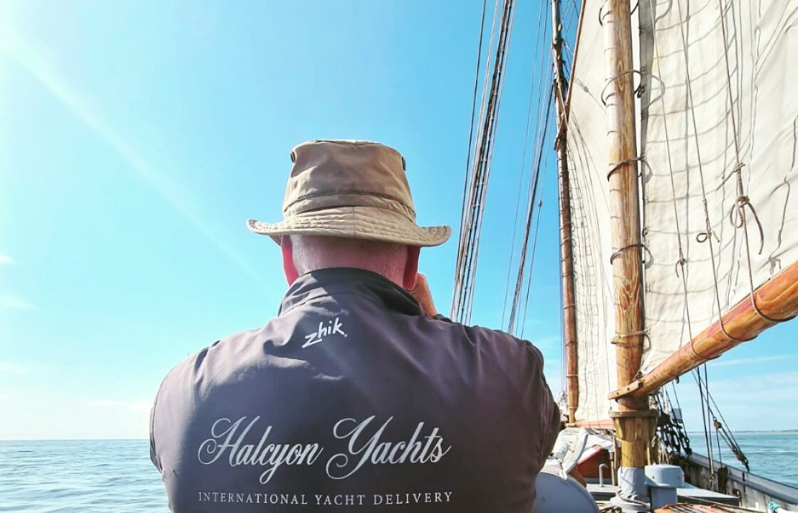 Professional yacht delivery crew showing the Halcyon Yachts logo on his back whislt sailing a classic yacht