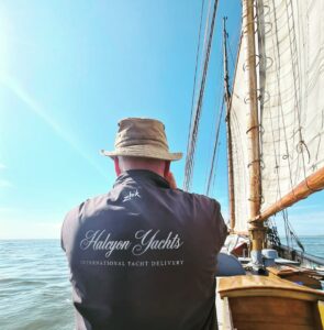Professional yacht delivery crew showing the Halcyon Yachts logo on his back whislt sailing a classic yacht